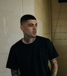 a man with tattoos standing in front of a brick wall and looking off into the distance