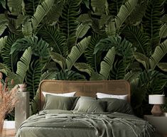 a bed with green sheets and pillows in front of a large plant wallpapered bedroom