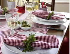 the table is set with red and white checkered placemats, plates, silverware, utensils and glasses