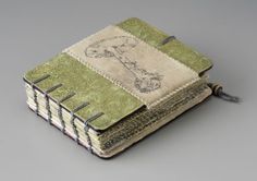 an old book is covered in green and white fabric with stitching on the pages