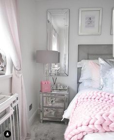 a bedroom with pink and silver decor on the bed, nightstands and mirror in the corner