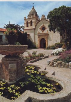 a building with a fountain and flowers in the foreground