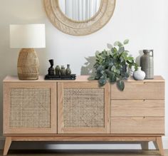 a sideboard with two drawers and a plant on it in front of a round mirror