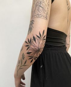 a woman's arm with tattoos on it and flowers in the middle, behind her