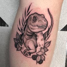 a black and white tattoo of a dinosaur with leaves around it's neck, on the leg