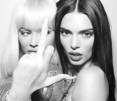 two women posing for the camera with one pointing at her finger and the other making a peace sign