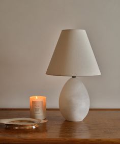 a table with a candle and a white vase on it next to a small mirror