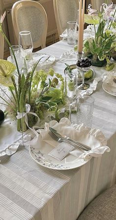 the table is set with plates, silverware and vases filled with greenery