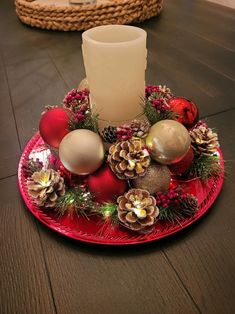 a candle is sitting on a red plate with christmas ornaments and pineconis around it