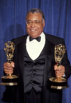 an older man in a tuxedo holding up two award trophies and smiling at the camera