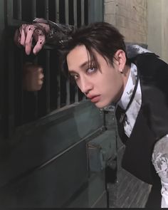 a man in a suit and tie leaning against a jail cell door with his hands on the bars