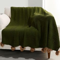 a couch covered with a green blanket and two brown pom poms on it