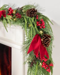 a christmas wreath with pine cones and red berries hanging from the mantel above a fire place