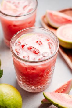 two glasses filled with watermelon juice next to sliced melons and limes