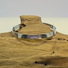 a silver bracelet sitting on top of a piece of wood with a metal bar in the middle