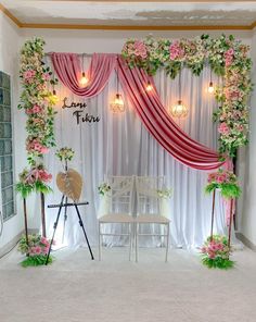 a decorated stage with pink flowers and greenery on the wall, white chairs and table