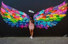 a woman standing in front of a wall with colorful wings painted on it's side