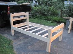 a wooden bed frame sitting on top of a parking lot next to a black truck