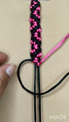 someone is making a cross with pink and black braiding on the end of it