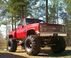 a large red truck parked in the middle of a forest with big tires on it