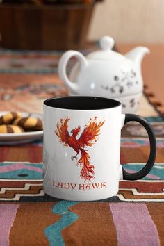 the lady hawk coffee mug is sitting on a table with cookies in front of it