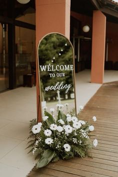 a welcome sign with flowers on the ground in front of a building that says, welcome to our wedding