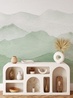 a shelf with vases and other items on it in front of a mountain mural