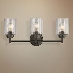 three light bathroom fixture with clear glass shades on the top and bottom lights in an antique bronze finish