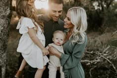 a man, woman and two children standing in front of trees with the sun behind them