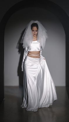 a woman in a white wedding dress and veil standing next to a wall with an arch