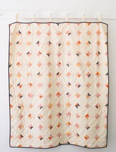 an orange and white quilt hanging on a wall next to a coat rack with hooks