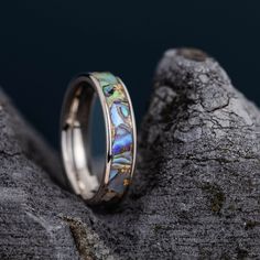 a wedding ring with an opalite inlay sitting on top of a rock