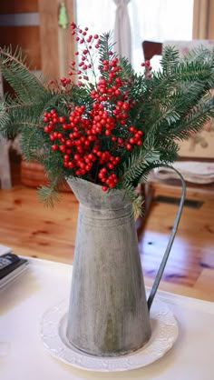 a metal pitcher filled with red berries and greenery