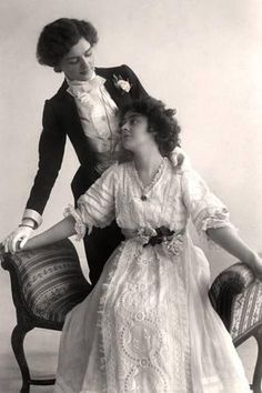 an old fashion photo of two women sitting on a chair, one wearing a dress