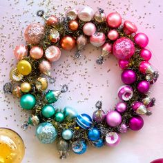 a wreath made out of christmas ornaments on top of a pink tablecloth with confetti