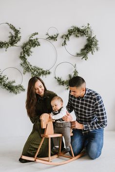 a man, woman and baby sitting on a rocking chair in front of a christmas tree