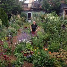 a woman standing in the middle of a garden filled with lots of plants and flowers