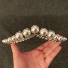 a woman's hand holding a silver brooch with pearls on it