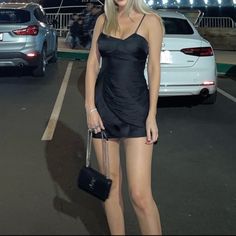 a woman in a short black dress is holding a purse and posing for the camera