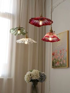 three lights hanging from a ceiling in a room with flowers and paintings on the wall