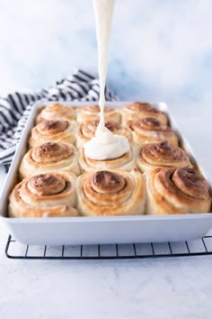 a pan filled with cinnamon rolls and cream being drizzled over the top