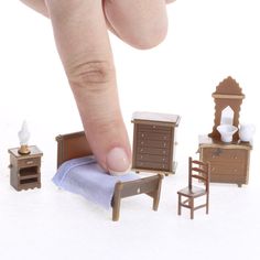 a finger touching a miniature bedroom set on a white surface with other furniture and accessories