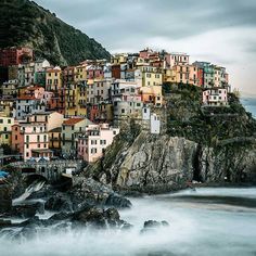 a small village on top of a cliff next to the ocean with boats in it