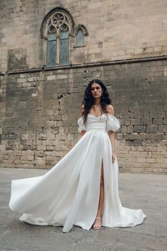 a woman standing in front of a brick building wearing a white dress