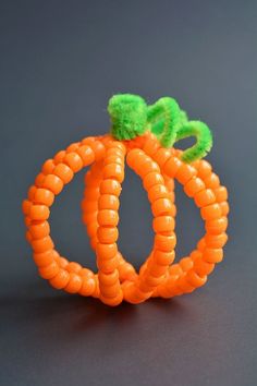 an orange and green ring made out of plastic beads on a black surface with a green pom - pom attached to it