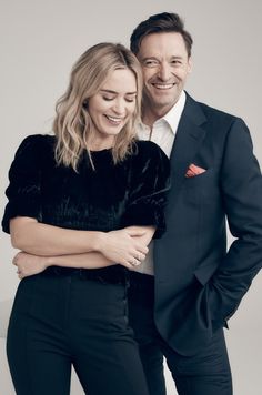 a man and woman standing next to each other in front of a white wall smiling