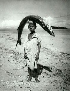 a young boy is standing on the beach with a fish in his hand and headband