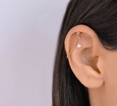 a woman's ear is shown with a single diamond in the middle and a gold chain around it