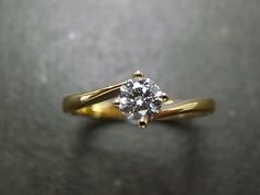 a yellow gold engagement ring with a single diamond on the top and bottom, sitting on a black surface