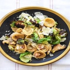 a black plate topped with pasta and broccoli on top of a white table cloth